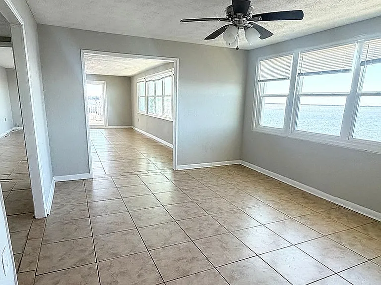 Bright and airy living space featuring large windows with stunning water views, tiled flooring, and a ceiling fan for comfort.