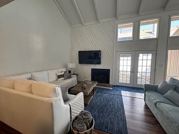 Modern living room, vaulted ceiling hardwood floors, fireplace, tv. Doors to patio.