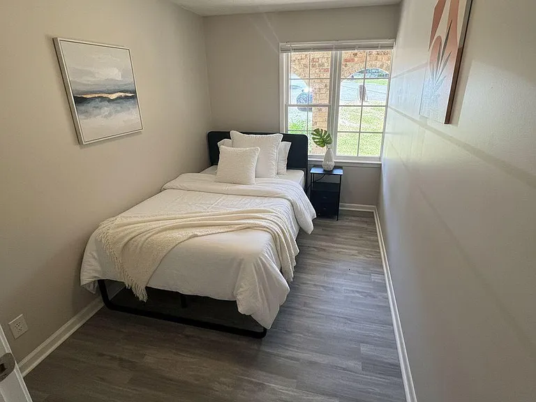 Private bedroom with a large window, durable plank flooring, and space for a bed and nightstand.
