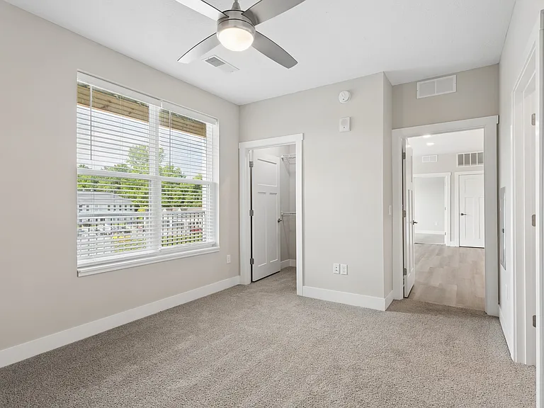 Carpeted bedroom and closet with ceiling fan of a Tiffany Flats apartment home.