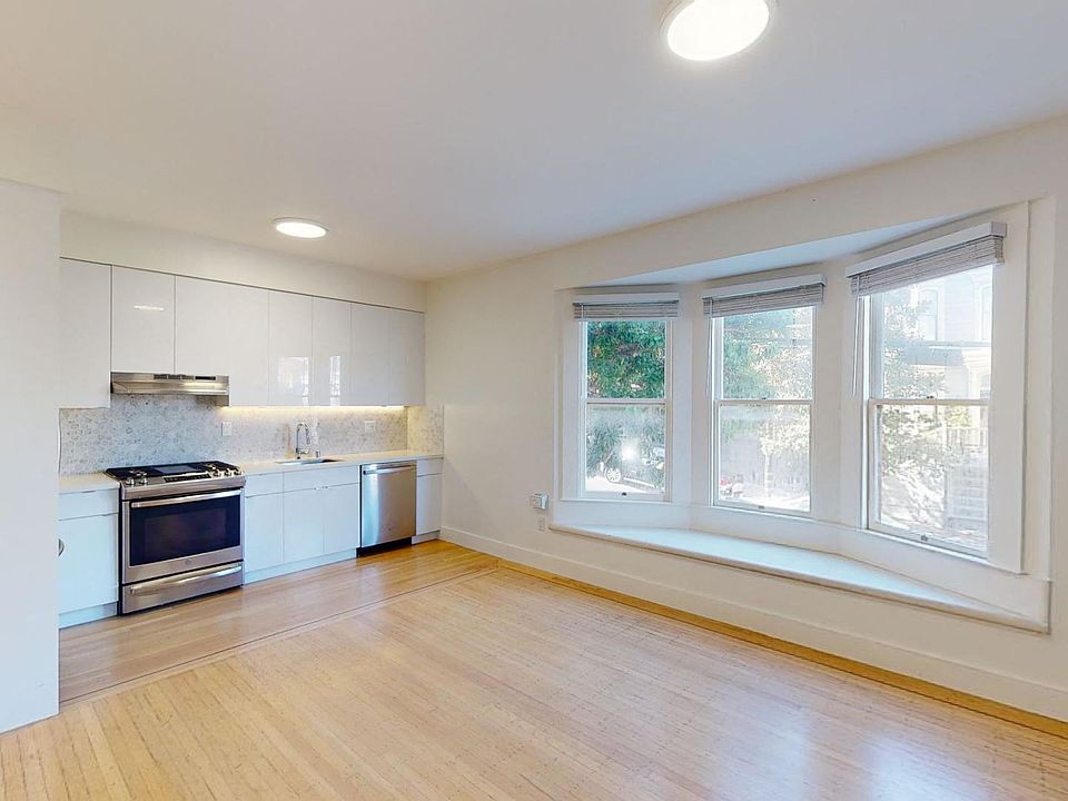 Spacious living room with a wood-like flooring, large window, and a view of the kitchen