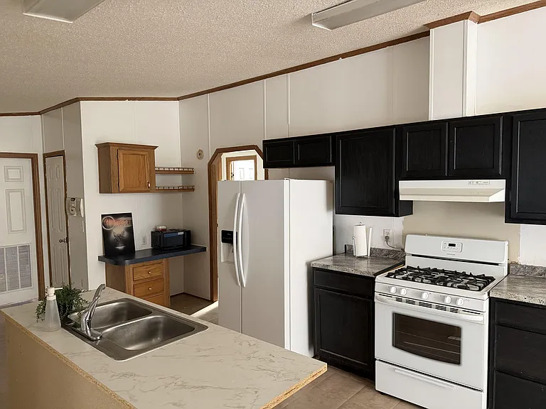 Functional kitchen with full-size refrigerator, gas range, ample cabinet storage, and a peninsula sink for meal prep.