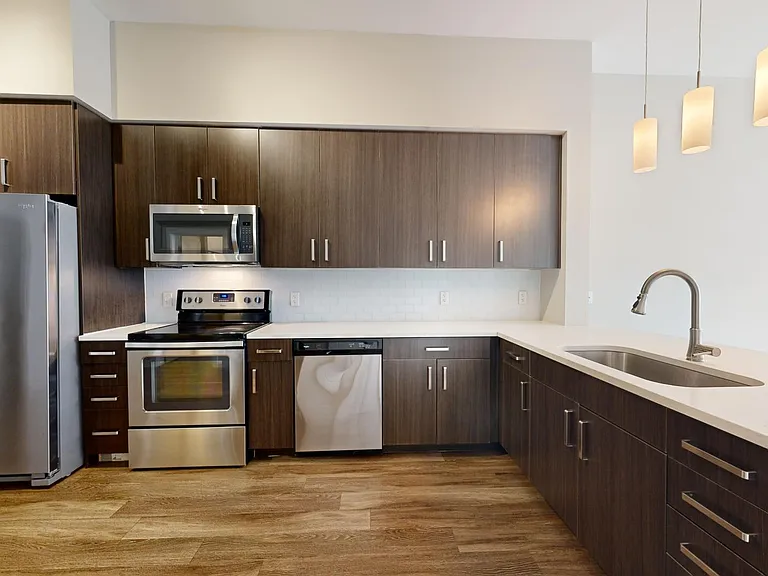 Apartment kitchen with stainless steel appliances, quartz countertops, and wood-style flooring.