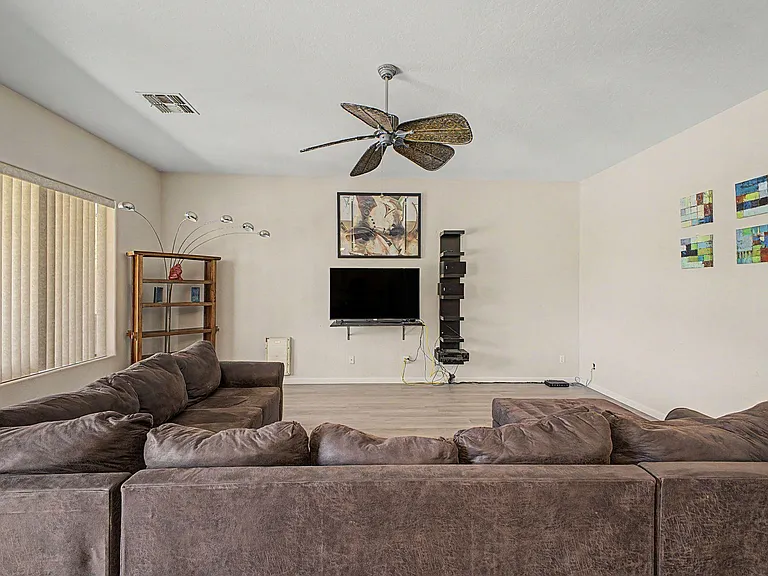 Spacious living room with ample seating, ceiling fan, and wall-mounted TV areaideal for relaxing or entertaining.