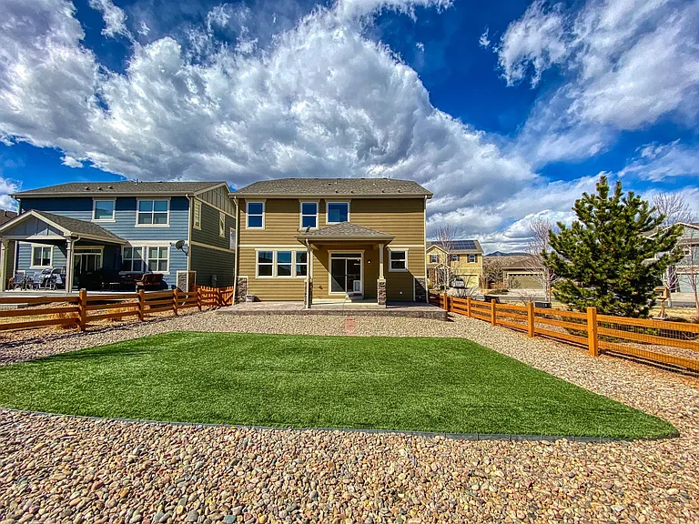 No-maintenance fenced-in backyard with realistic artificial grass, river rock, covered patio, natural gas line for grill, and views of North Table Mountain.