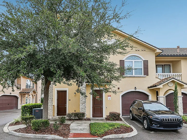 Charming townhouse with classic architecture, lush greenery, and attached garage in a serene neighborhood setting.