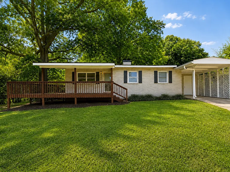 Single-story brick home with raised front deck, one-car carport and additional driveway parking.
