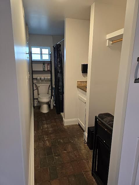 Toilet, bathroom, shower, vanity and open closet with brick pavers