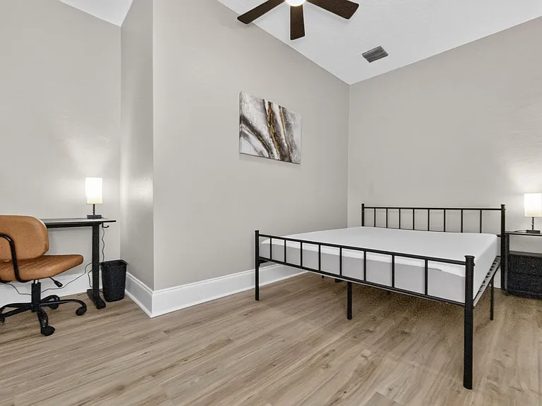 Spacious bedroom with metal bed frame, nightstands, ceiling fan, and a dedicated desk area for work or study.