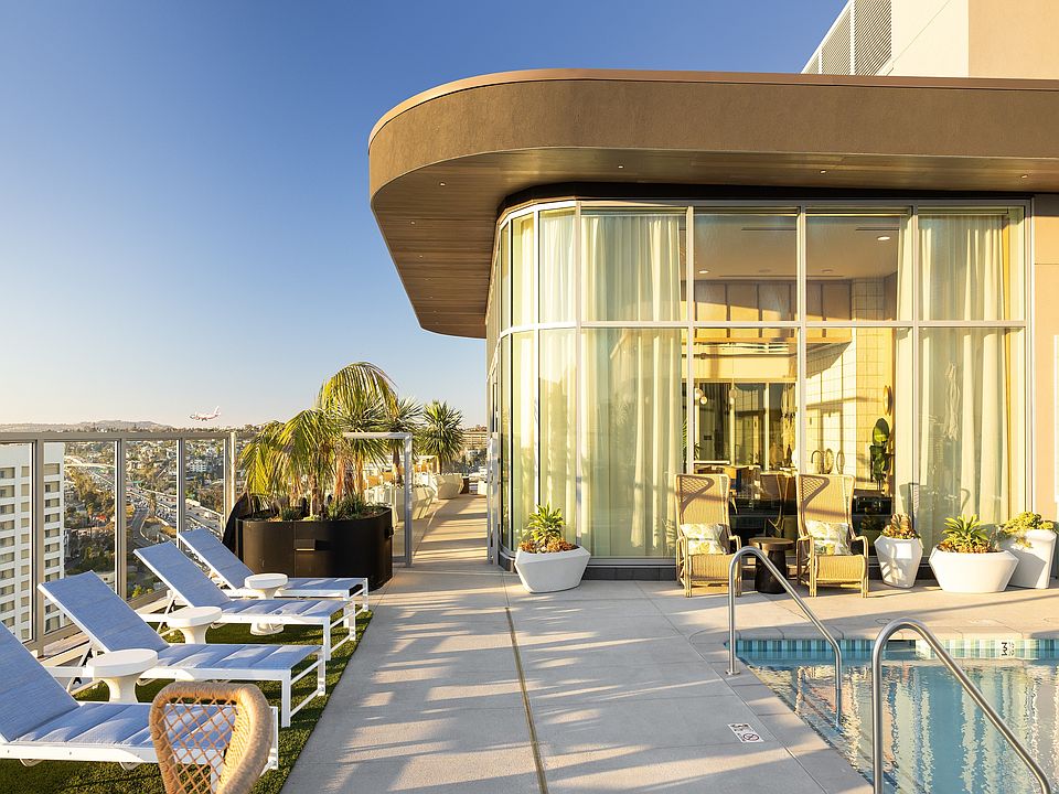 Luxurious rooftop pool area with sleek lounge chairs, panoramic city views, and modern glass-encased lounge in a vibrant high-rise setting.