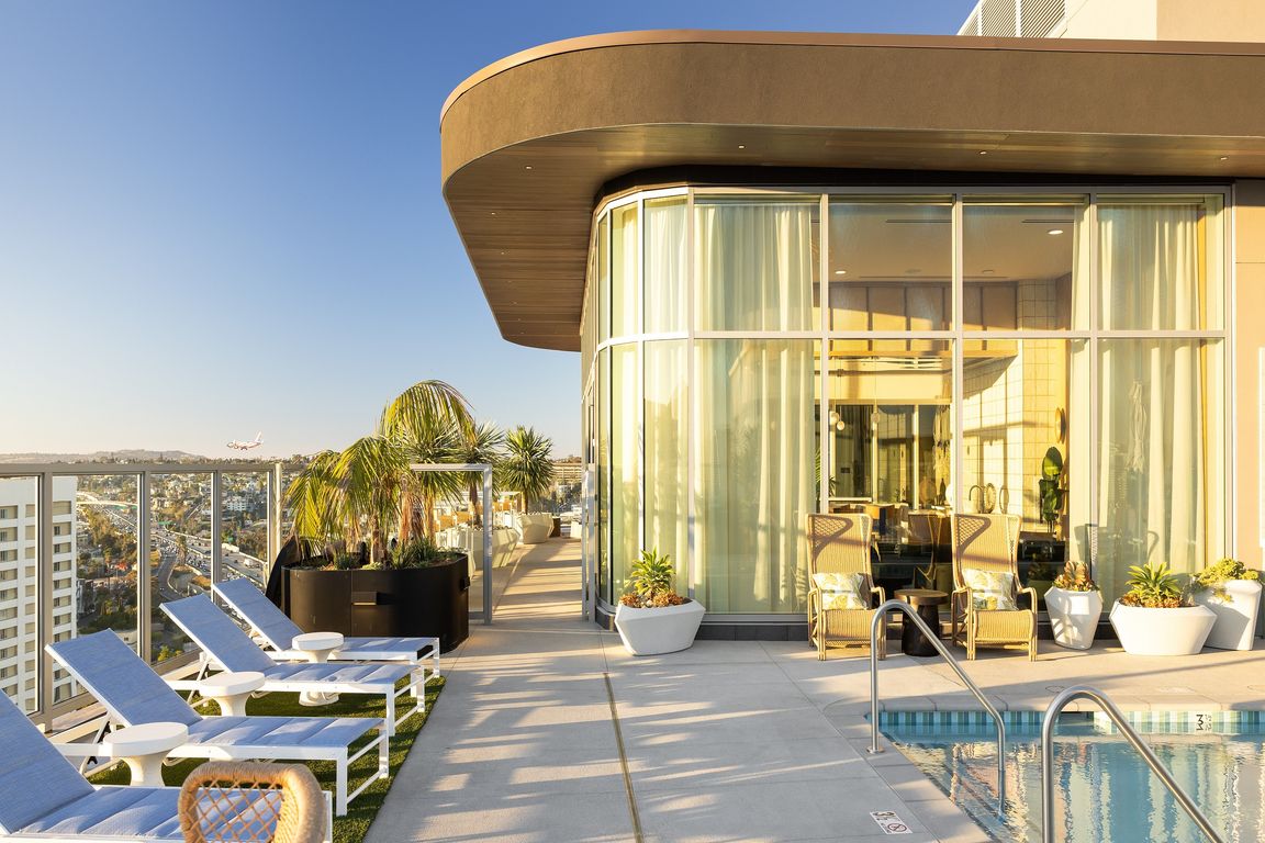 Luxurious rooftop pool area with sleek lounge chairs, panoramic city views, and modern glass-encased lounge in a vibrant high-rise setting.