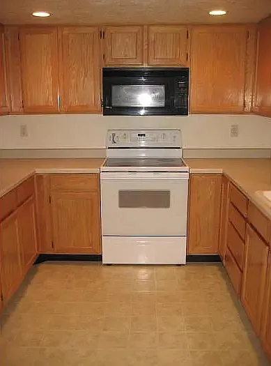 Kitchen with white electric range oven, black microwave, light countertops, and recessed lighting