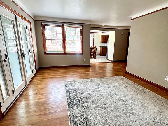 Living room, with hardwood floors and cove ceilings, is well lit with natural light from double windows and large French doors.