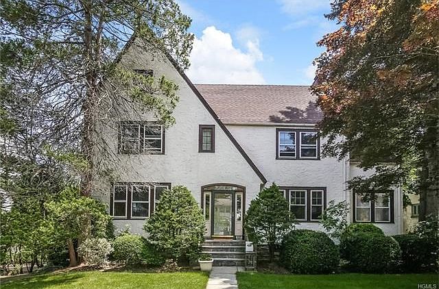 Front of house with lush, landscaped green lawn and manicured plantings.