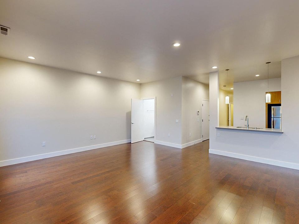 Living room with a large window, wood-like flooring, and entrance to the kitchen