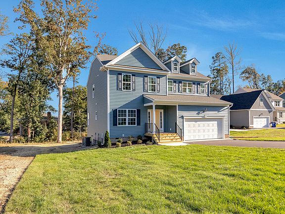 Charming two-story blue home on Lot 29 in Poplar Village, featuring white trim, garage, and lush gre