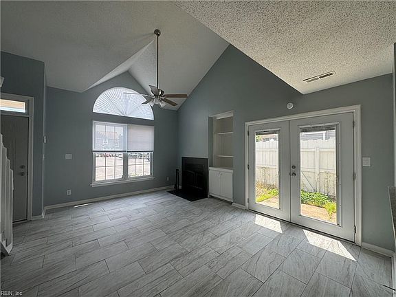 Living room features high vaulted ceilings, a cozy fireplace, and charming French doors that open to the back porch.