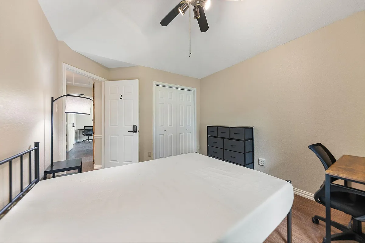 Photo 2 of 9 - Debbie Cir - Rowlett, TX Furnished bedroom featuring a bed, dresser storage, and a work desk, plus a sliding-door closet and ceiling fan. - Debbie Cir