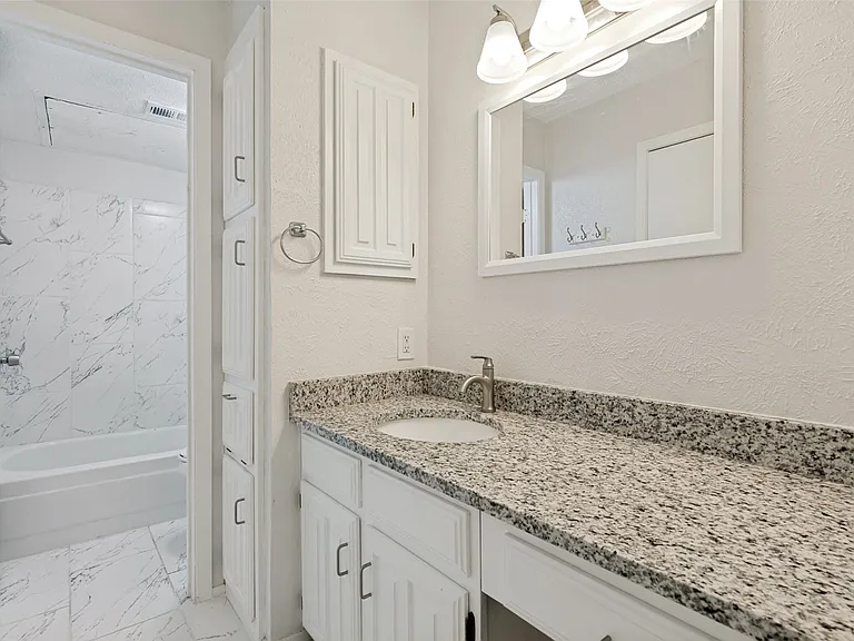 Bathroom vanity featuring a speckled countertop, undermount sink, and white cabinetry