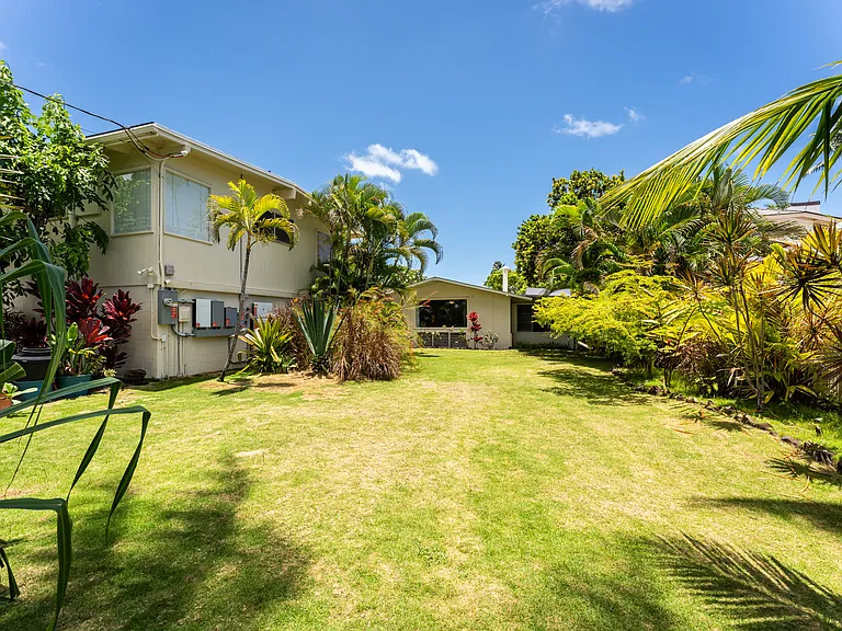 Large front yard with tropical landscaping and additional gated property access.