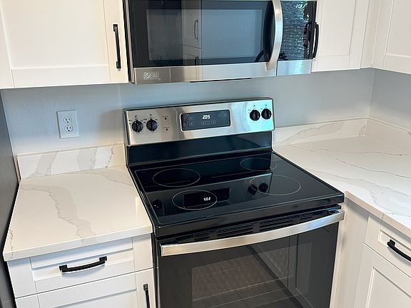 Kitchen has luxurious quartz countertops and features a glass top stainless steel stove paired with a matching microwave.