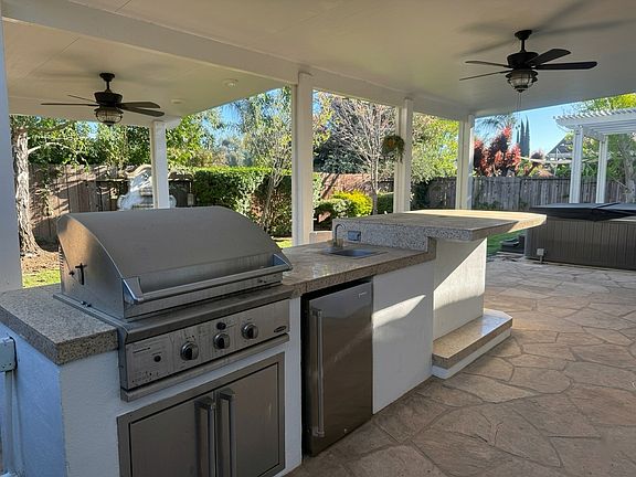 Built-in outdoor kitchen with gas grill, sink, and refrigerator under a covered patio with ceiling fans _ perfect for year-round entertaining.