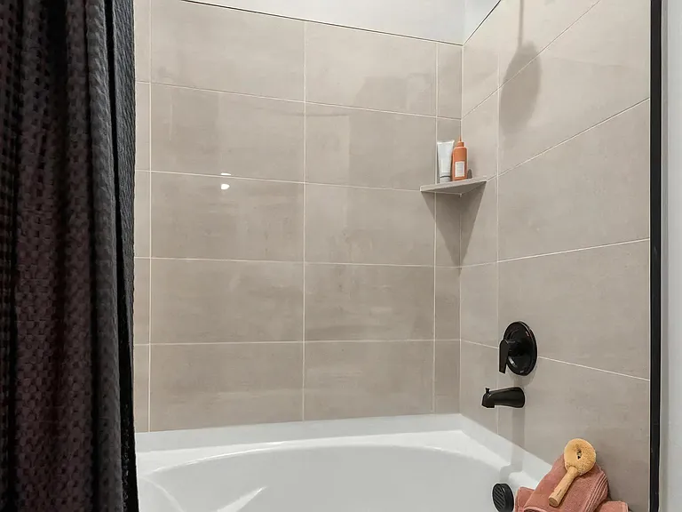 Beige Tile Bathtub Wall with Shower Fixtures and Built-In Shelf