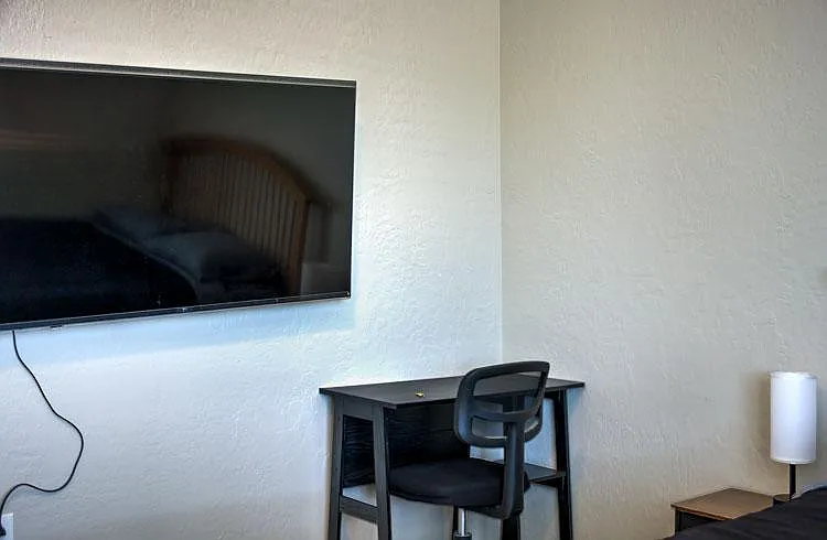 Bedroom setup includes a wall-mounted TV and a compact desk area, plus bedside table lighting for everyday use.