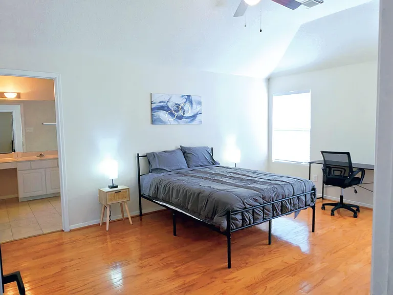 Spacious bedroom with hardwood floors, ceiling fan, work desk, and direct access to a private vanity/bath area.