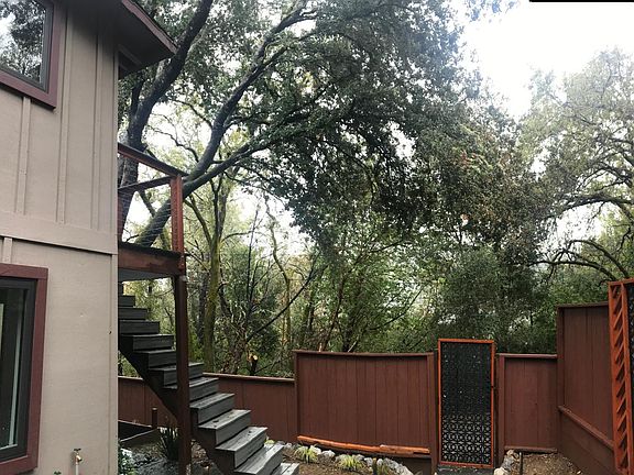 Custom landscaping & outdoor lighting with beautiful outdoor patio & staircase leading to large upstairs deck & front door.