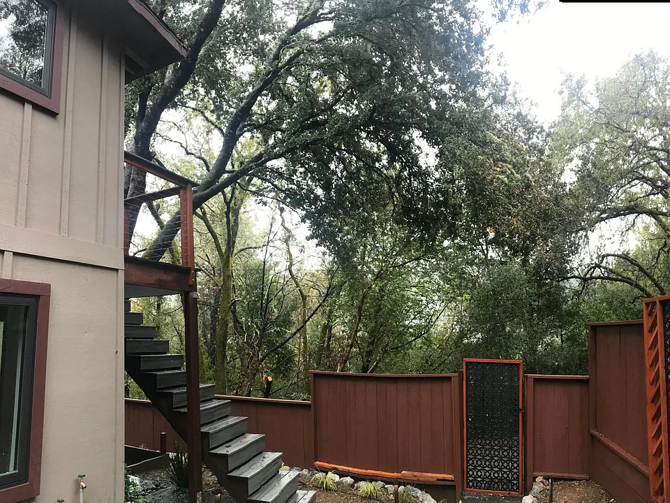 Custom landscaping & outdoor lighting with beautiful outdoor patio & staircase leading to large upstairs deck & front door.