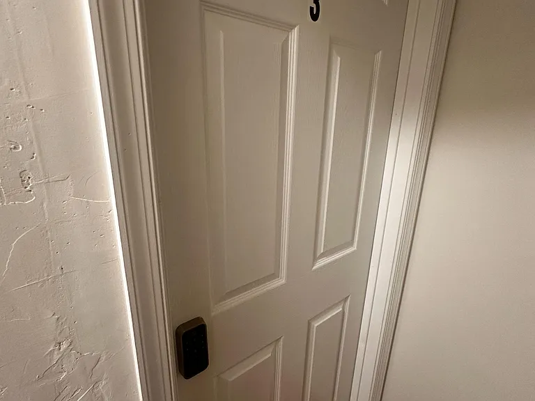 Secure interior entry with keypad lock and numbered door, set along a clean hallway with wood-look flooring.