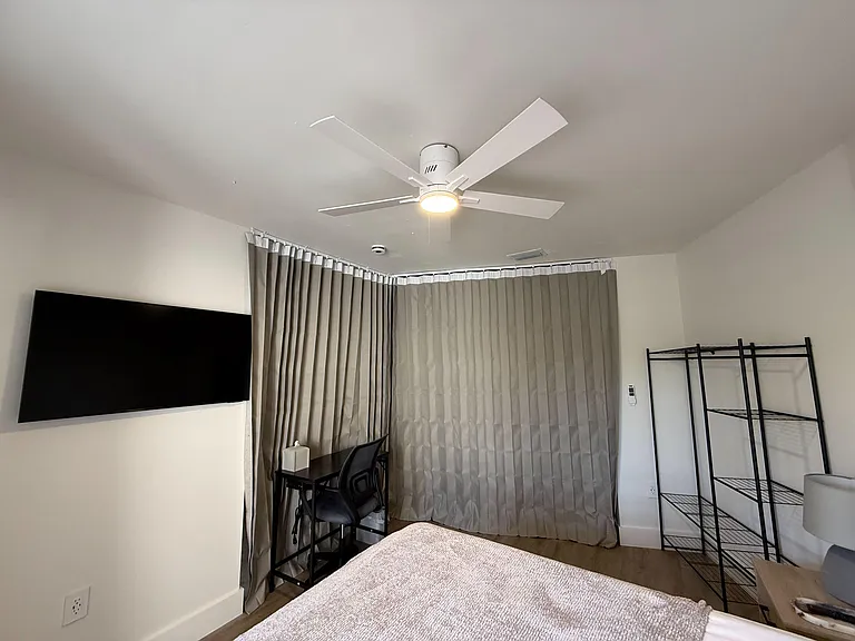 Bedroom includes a ceiling fan, full window coverage with drapery, and space for a bed, desk, and storage shelving.
