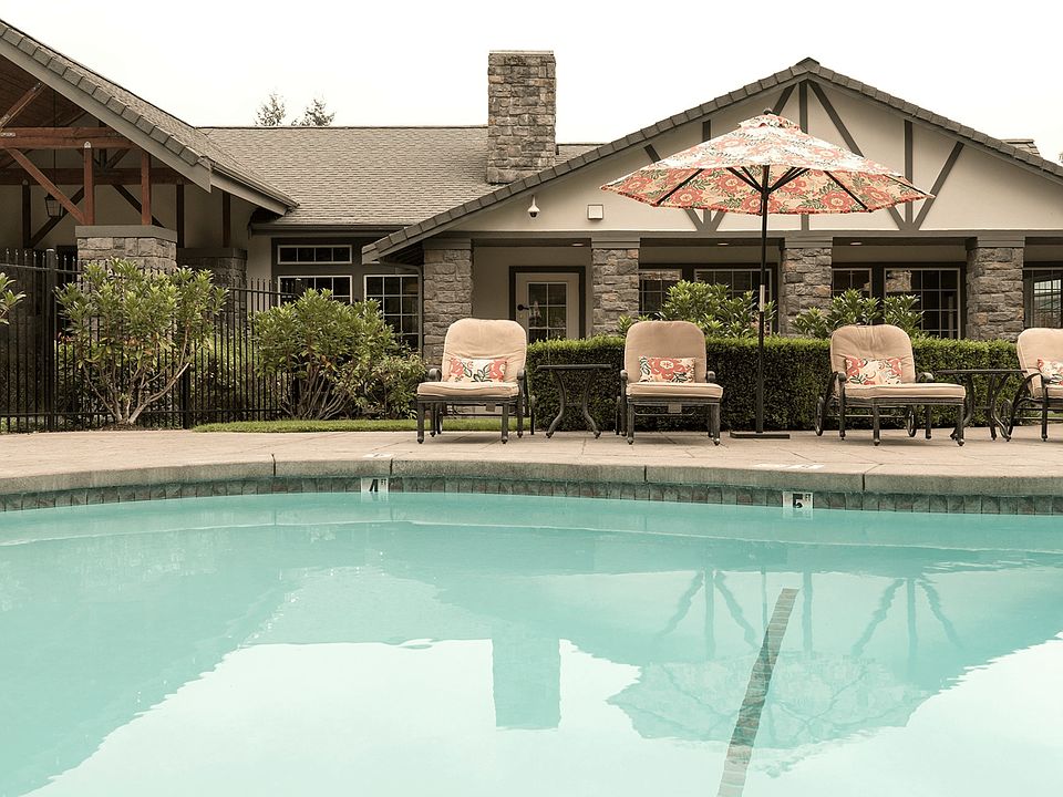 Elegant apartment complex with cozy outdoor seating by a refreshing pool, surrounded by lush greenery and rustic architecture.