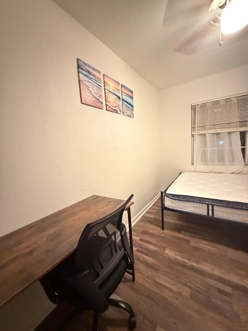 Private bedroom with wood-style flooring, a work desk and chair, and space for a full bed near a window with blinds. - E 112th Ave
