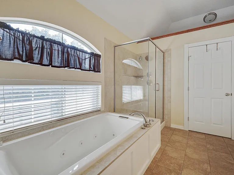 Primary Bathroom featuring a jetted tub with tile surround, a separate glass-enclosed shower, dual counters, private water closet, ample light and one of the two primary closets