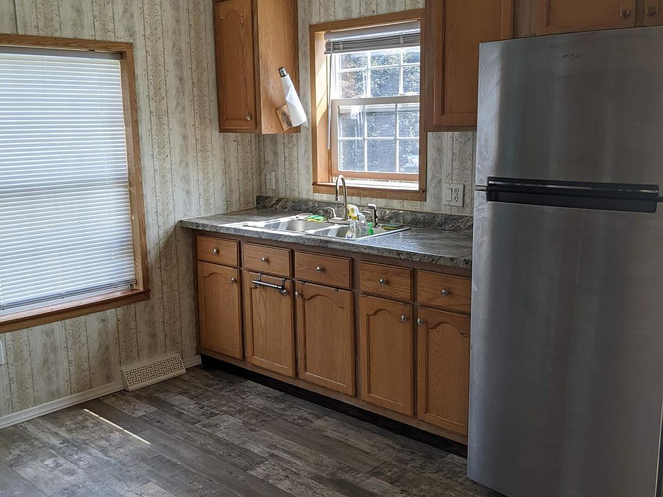 Kitchen area. Two windows in front of unit face the road. Newer stainless refrigerator and newer countertop. Vaulted ceiling in kitchen. Laminate floor. Mini blinds on windows.