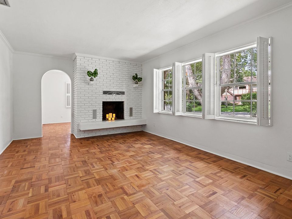 This mid century home features parquet floors, archways, colored tile, custom window shutters and a painted brick decorative fireplace.