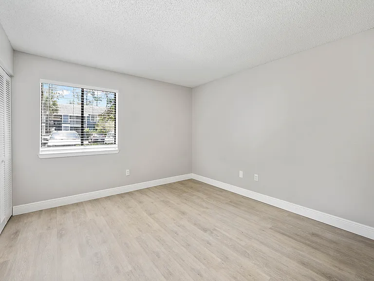 Bright and spacious bedroom with modern laminate flooring, large window with a view, and clean white walls.