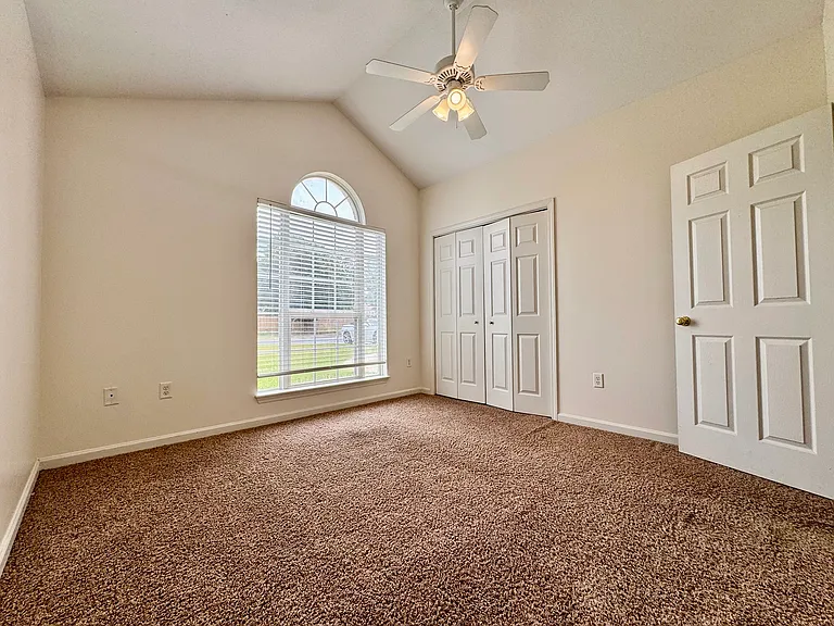Secondary bedroom with vaulted ceiling, ceiling fan, closet, and arched window