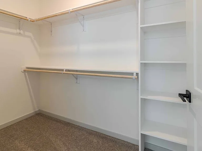 Spacious walk-in closet with built-in shelving and dual hanging rods for ample storage. Spacious walk-in closet with built-in shelving and dual hanging rods for ample storage.