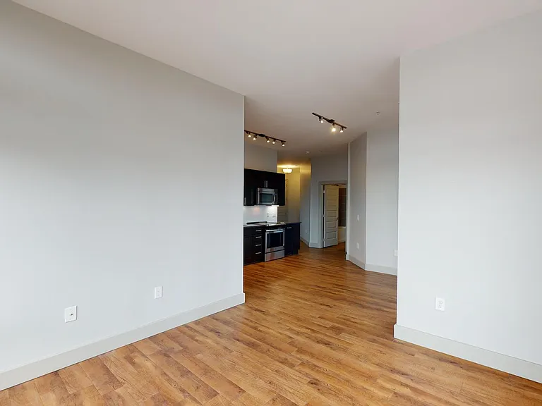 Apartment kitchen with stainless steel appliances, dining and living room with wood-style flooring.