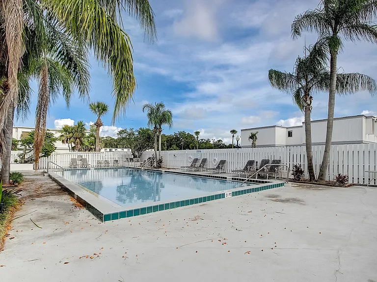 Inviting outdoor pool area with clear blue waters, surrounded by lush palm trees and modern lounge chairs, perfect for relaxation.