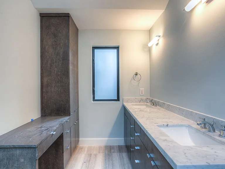 Master bath with dual Carrara marble vanity, undermount sinks, walnut-stained cabinets, and a frosted privacy window