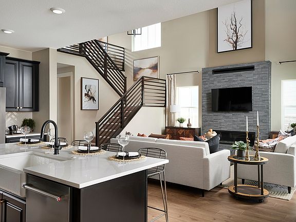 A modern and open-concept living space with a kitchen island, a fireplace, and a staircase with a un