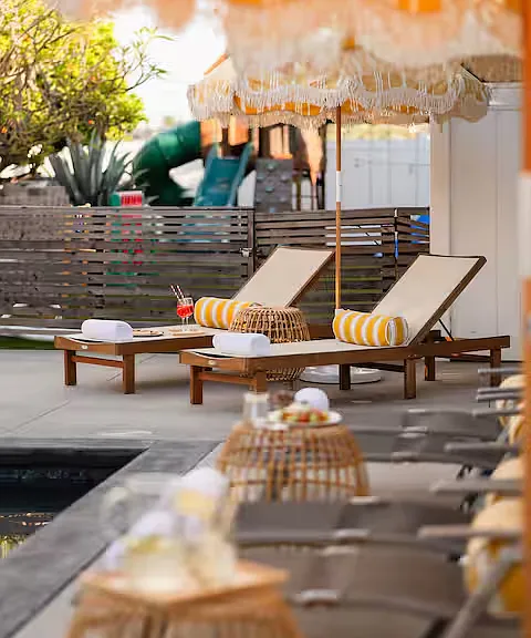 Resort-style outdoor space with a heated pool, hot tub, sun loungers with umbrellas, and cozy seating. Perfect for relaxing, sunbathing, or enjoying poolside drinks, this stylish area offers a luxurious retreat for ultimate leisure.