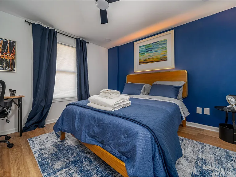 Furnished bedroom with a full bed, desk workspace, and window with curtains, plus hardwood-style floors and ceiling fan.