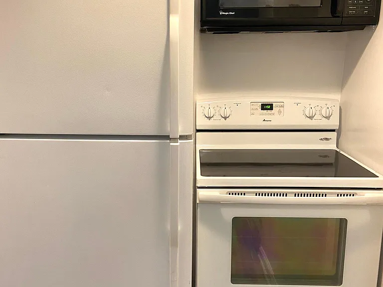 View of kitchen appliances, refrigerator, electric flat top stove/range and microwave.