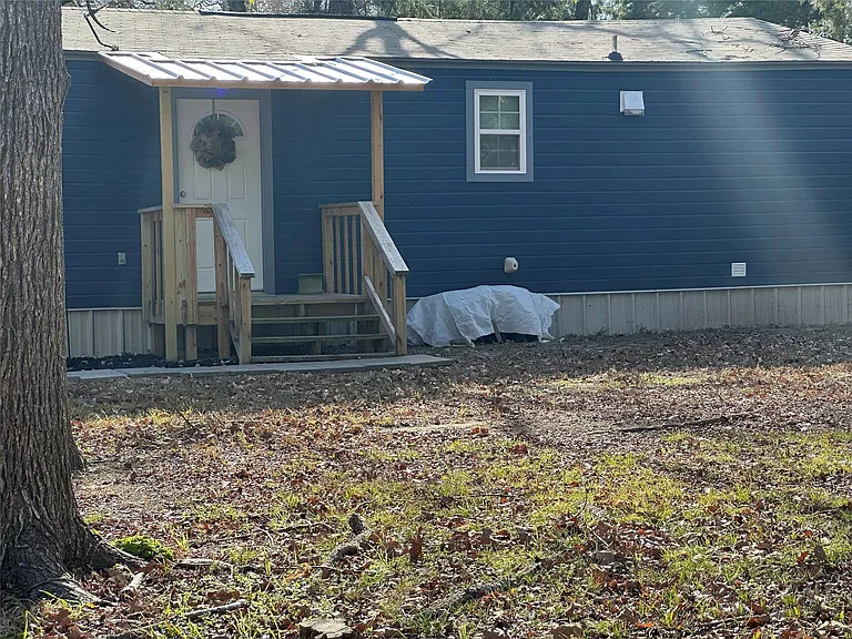 Blue horizontal siding exterior with a white entry door, covered porch, wood porch railing, and a single window with white trim