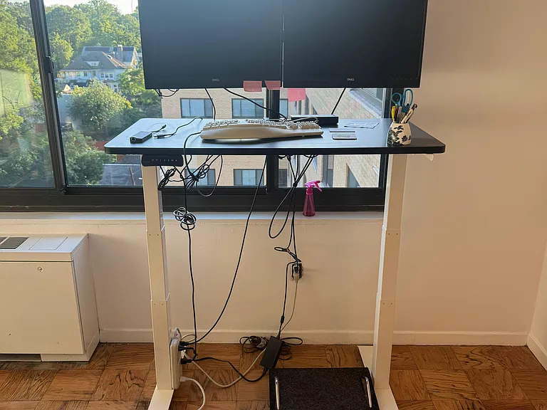 Flexispot adjustable sit/stand desk with two monitors and external keyboard and docking station.